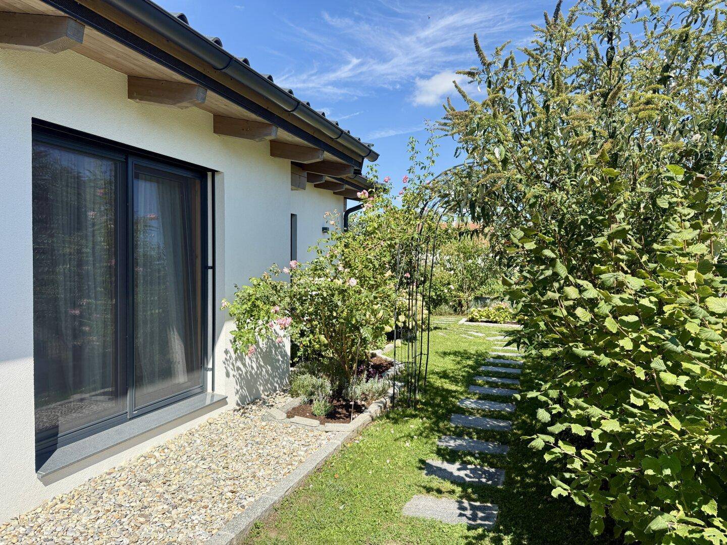 Nahaufnahme eines Fensters mit Kiesbeet und einem gepflegten Gartenweg daneben unter blauem Himmel.