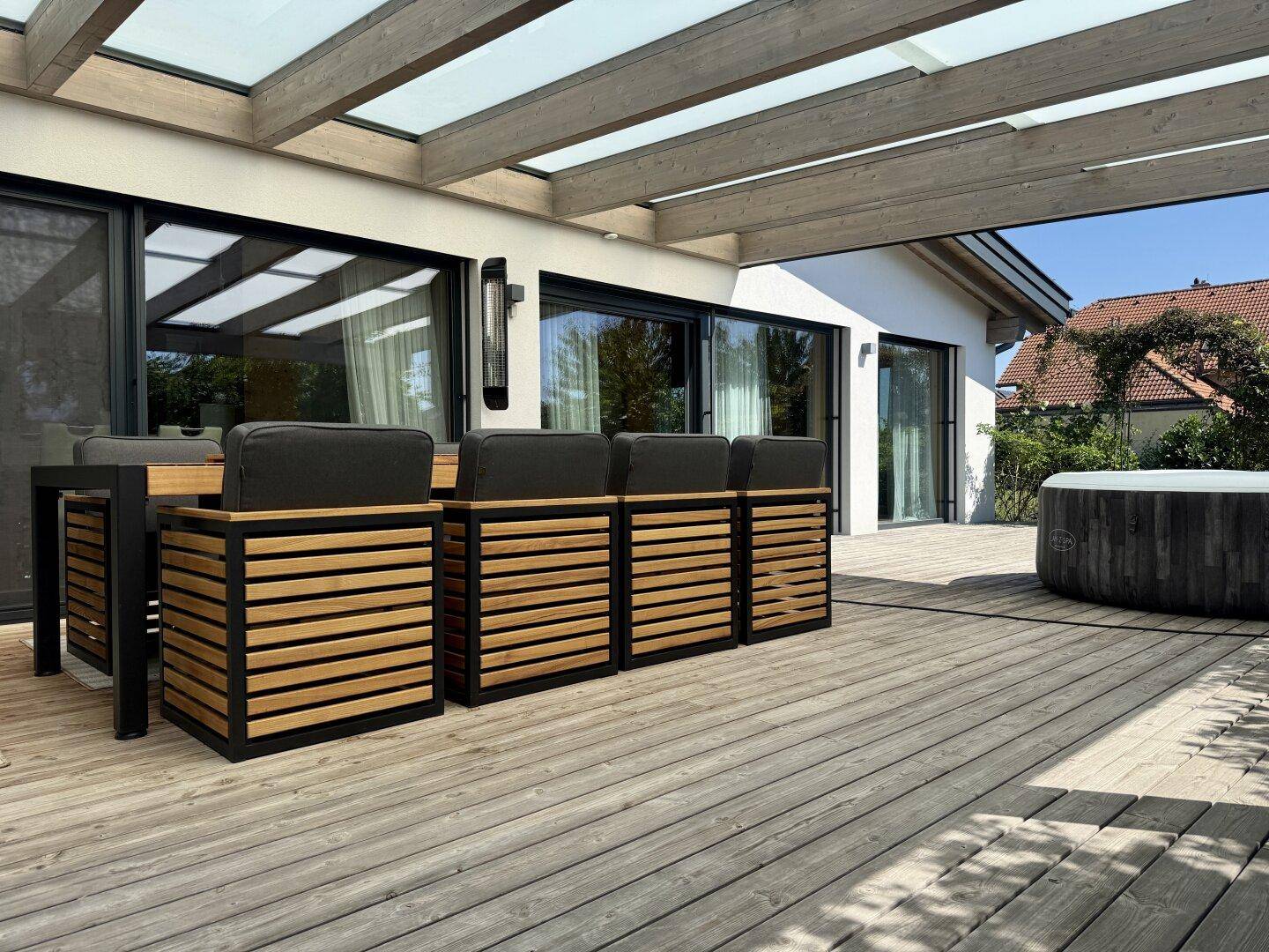 Weitläufige Holzterrasse mit modernem Essbereich und Whirlpool, umgeben von viel Grün.