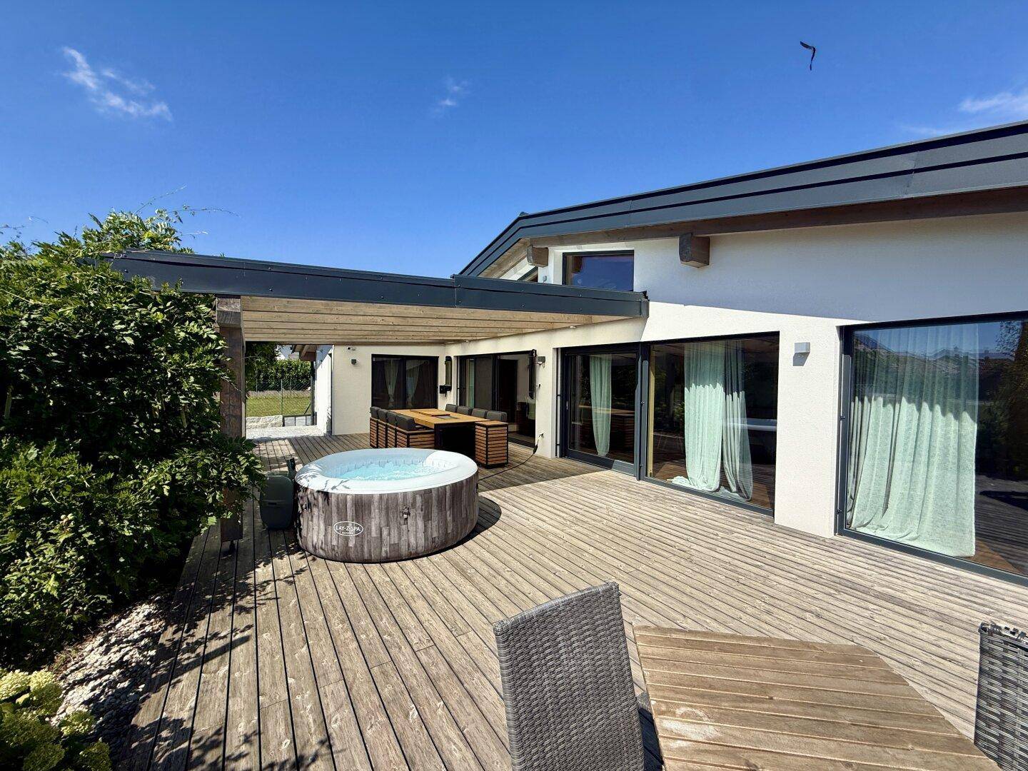 Große Holzterrasse mit Whirlpool und Essbereich, direkt am modernen Haus gelegen.