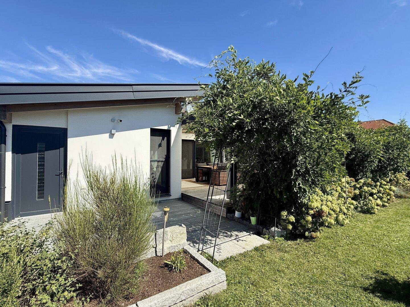 Gepflegter Gartenbereich neben dem Haus mit Sträuchern und einem Zugang zur Terrasse.