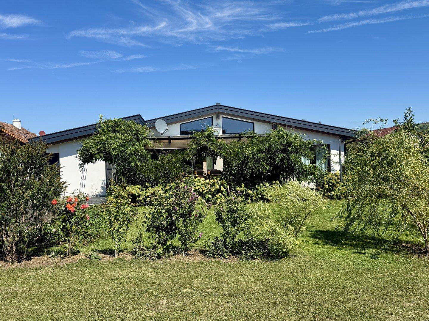 Modernes Einfamilienhaus mit Flachdach und großen Fenstern, umgeben von einem grünen Garten.