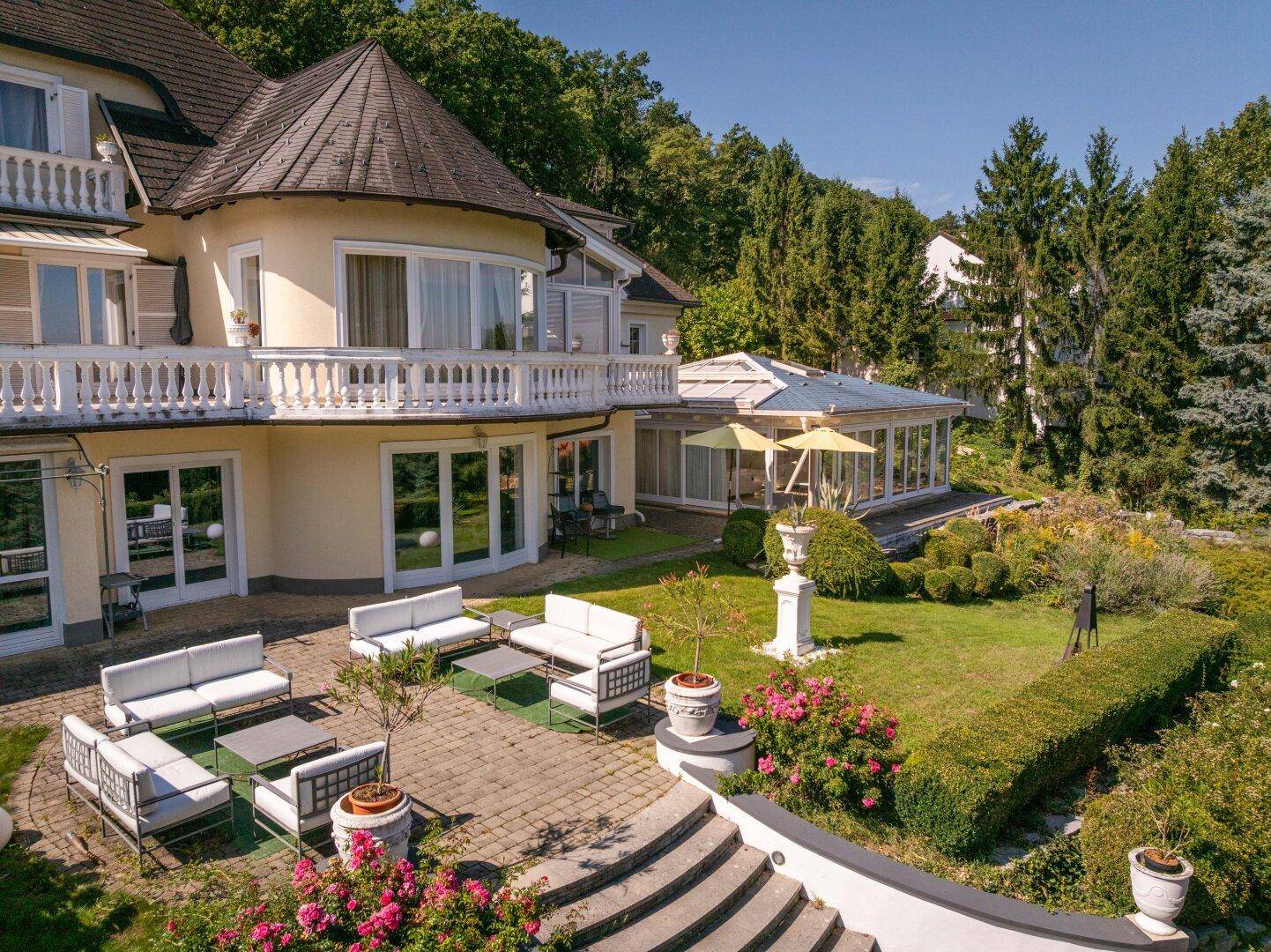 Große gepflasterte Terrasse mit modernen Gartenmöbeln und Blick ins Grüne.