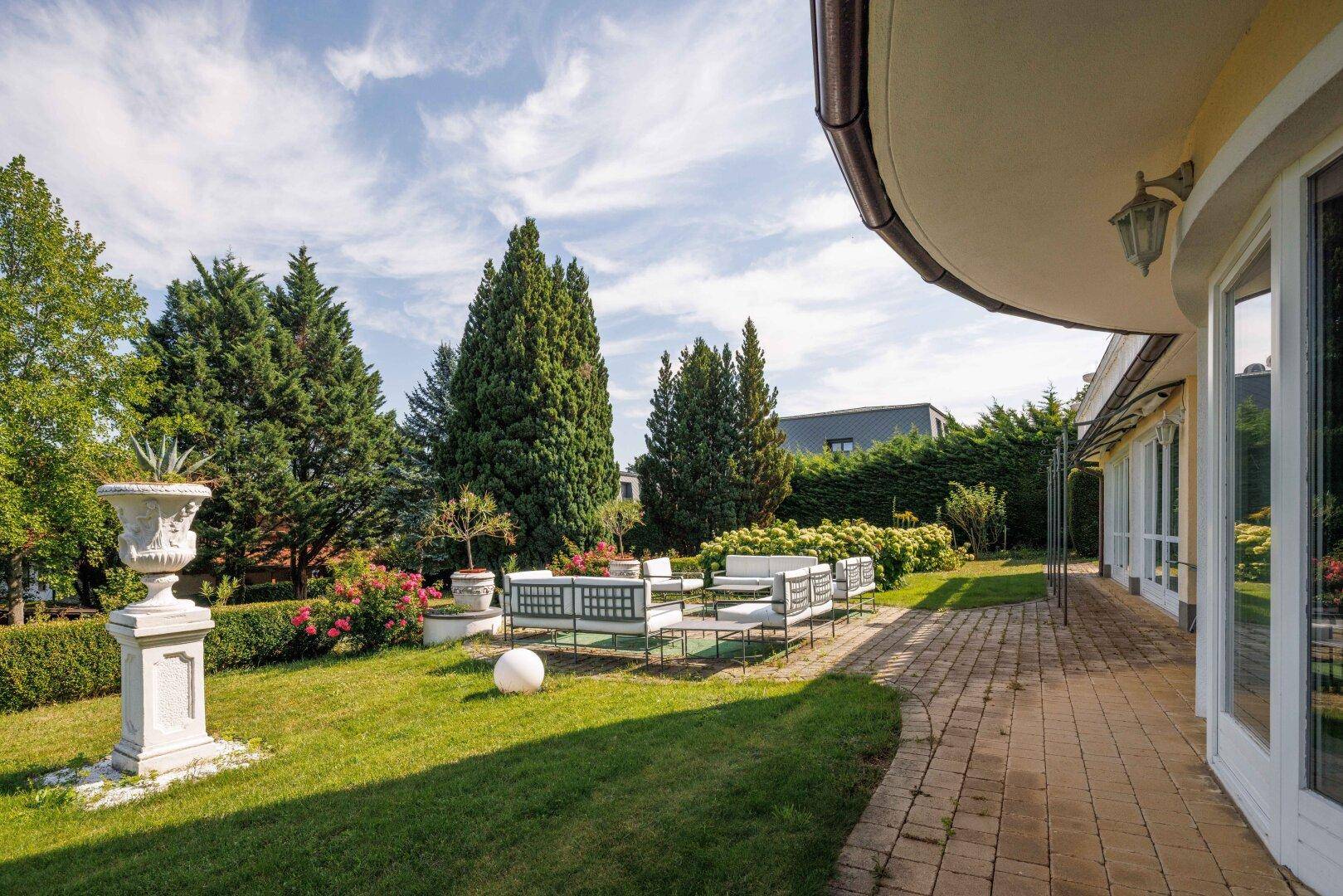 Sonniger Gartenbereich mit gepflasterter Terrasse und modernen Lounge-Möbeln.