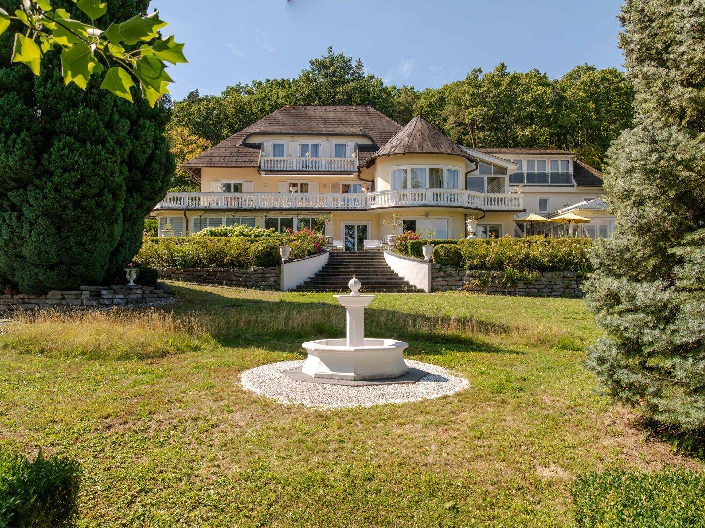 Weitläufiger Garten mit Rasenfläche, Zierbrunnen und altem Baumbestand.