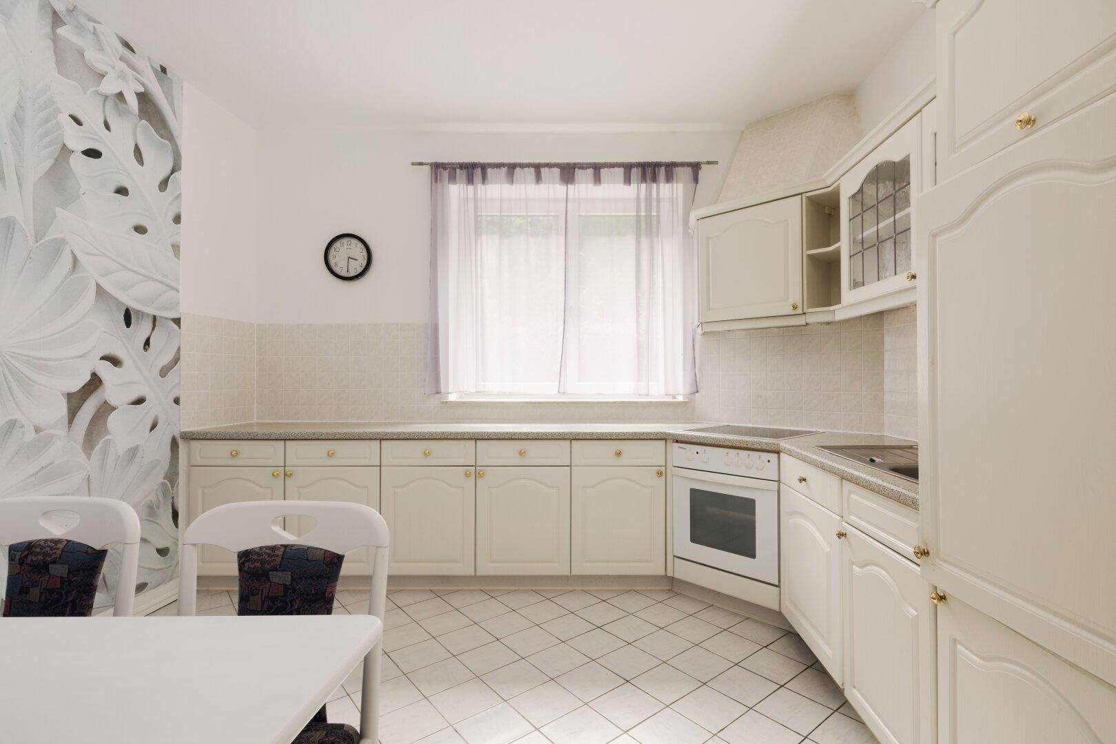 Helle Küche im Landhausstil mit weißen Schränken, Fliesenboden und Fenster.