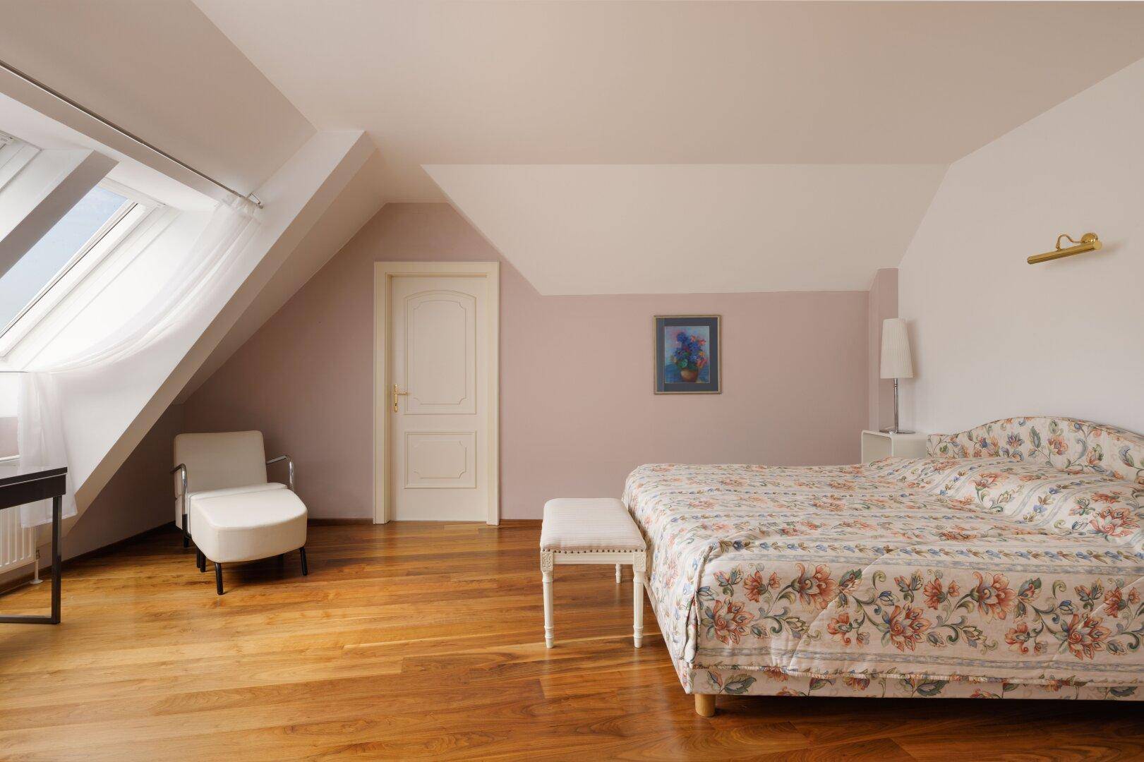 Helles Schlafzimmer im Dachgeschoss mit Holzboden, Dachfenster und schrägen Wänden.