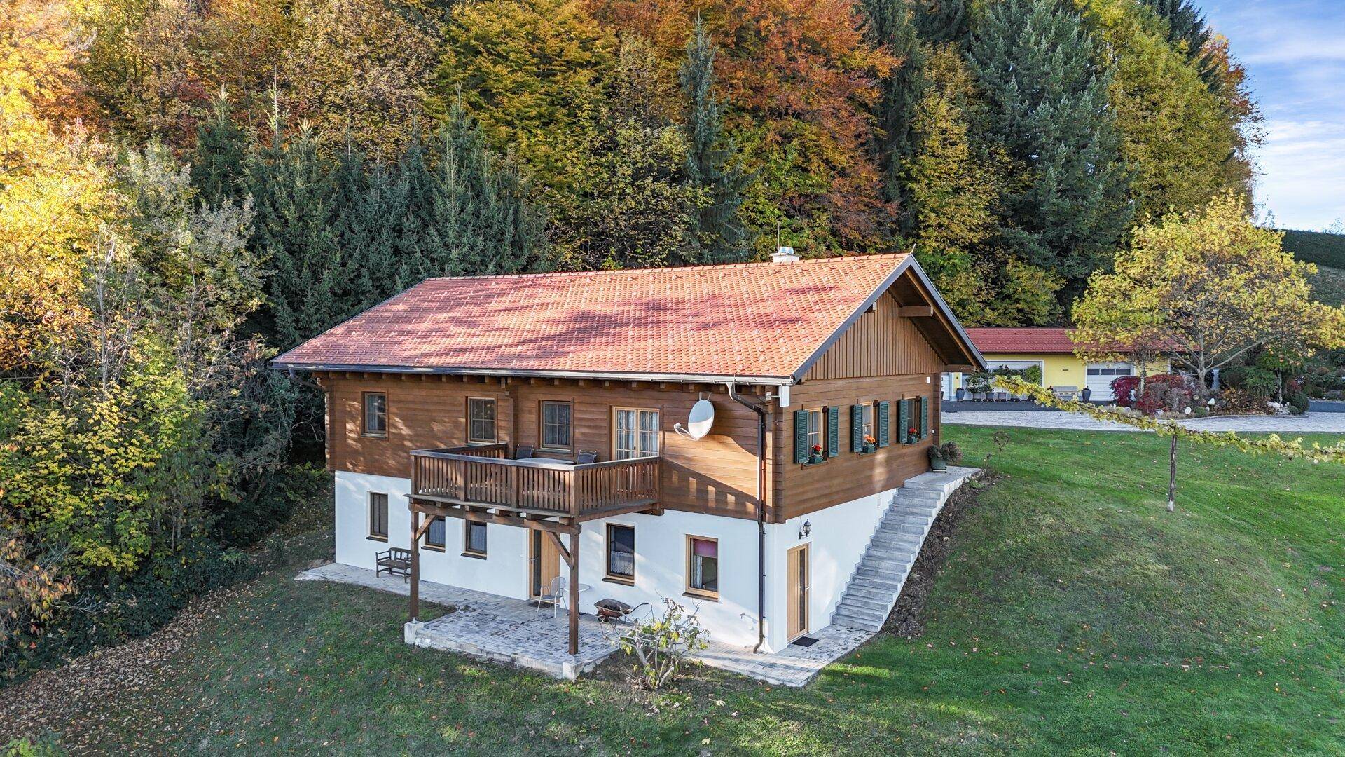 Rustikales Holzchalet mit Balkon, umgeben von Bäumen und einer grünen Wiese.