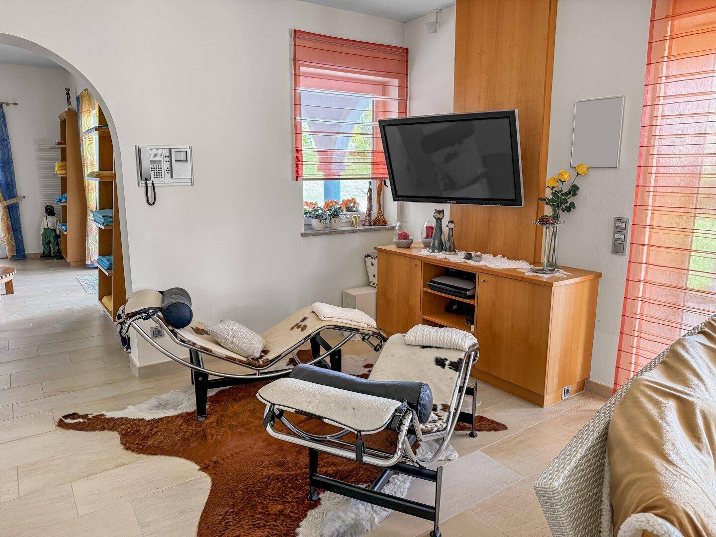 Gemütlicher Wohnbereich mit Fernseher, Liegen und Kuhfellteppich auf Fliesenboden.