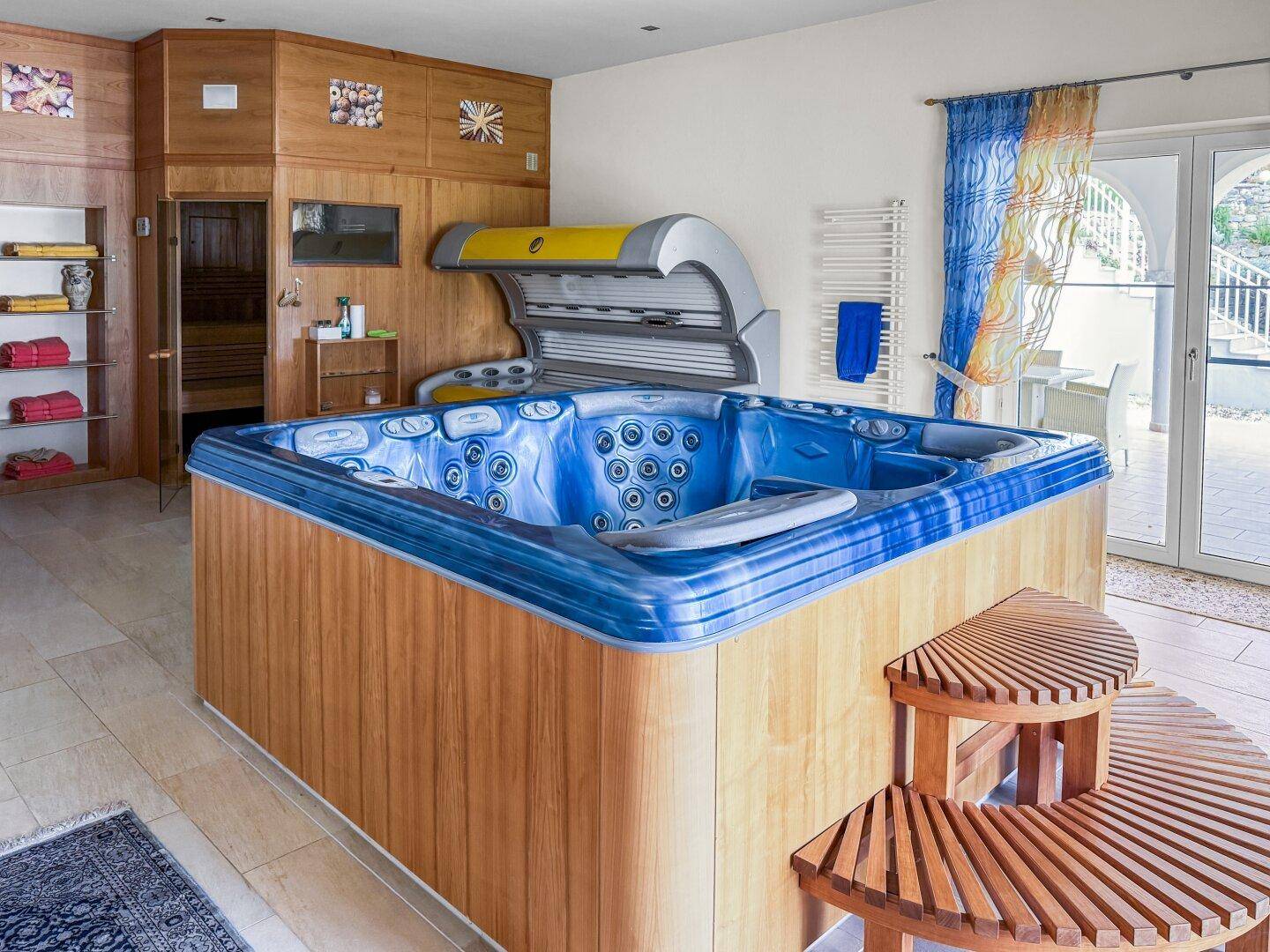 Innenbereich mit großem Whirlpool, Solarium und Holzwänden, mit Zugang zur Terrasse.