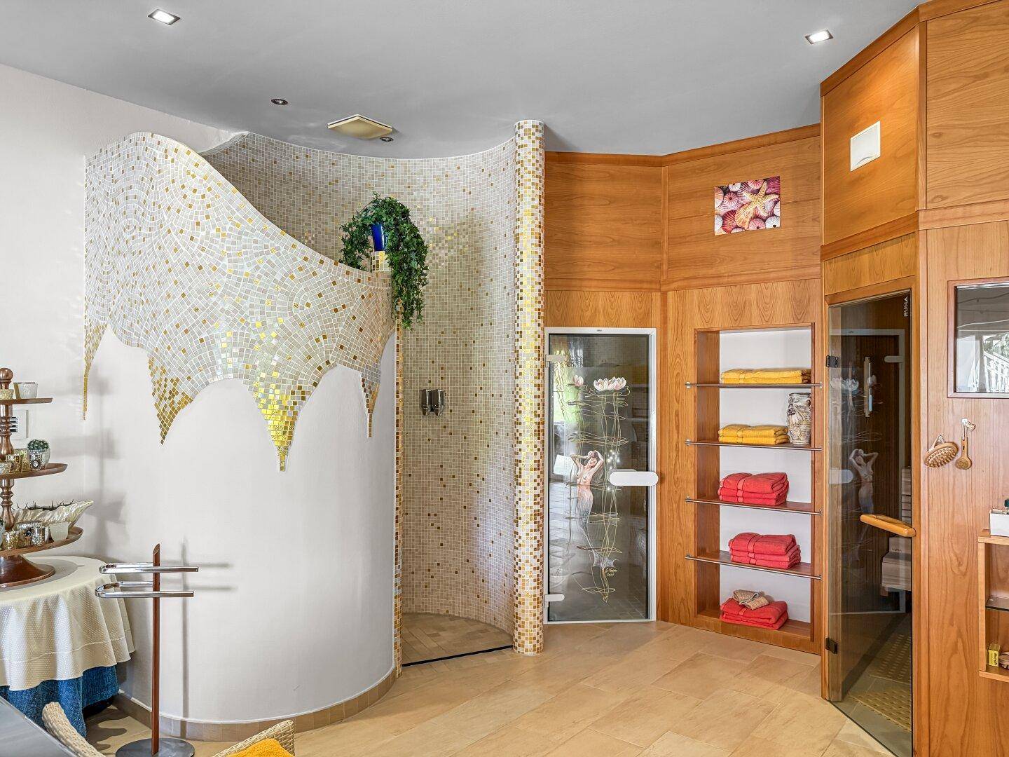 Stilvoller Wellnessbereich mit Mosaikdusche, Sauna und Holzverkleidung.