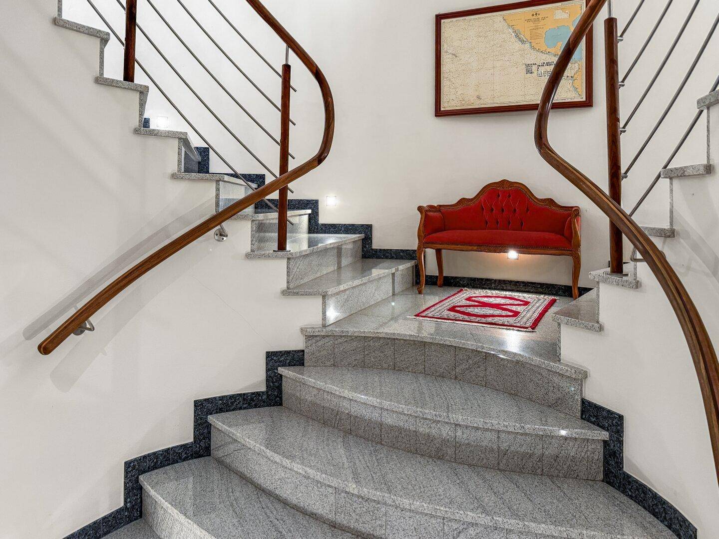 Elegante Treppe mit Granitstufen, Holzgeländer und roter Samtbank.