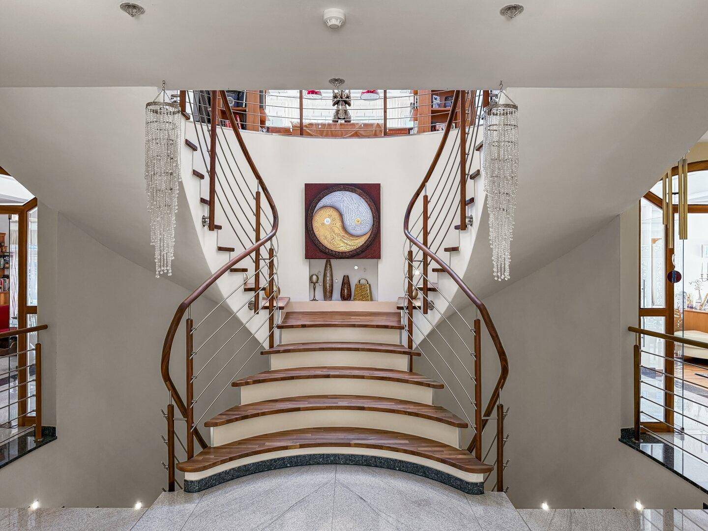 Geschwungene Treppe mit Holzgeländer, Edelstahlstäben und eleganten Kronleuchtern.
