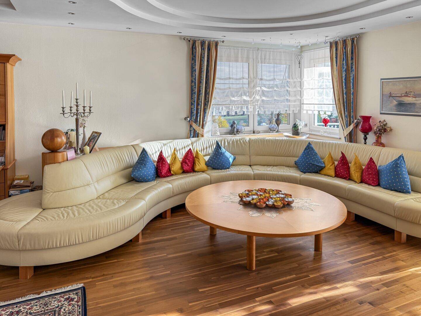 Helles Wohnzimmer mit großem beigem Sofa, Holztisch und vielen Kissen.