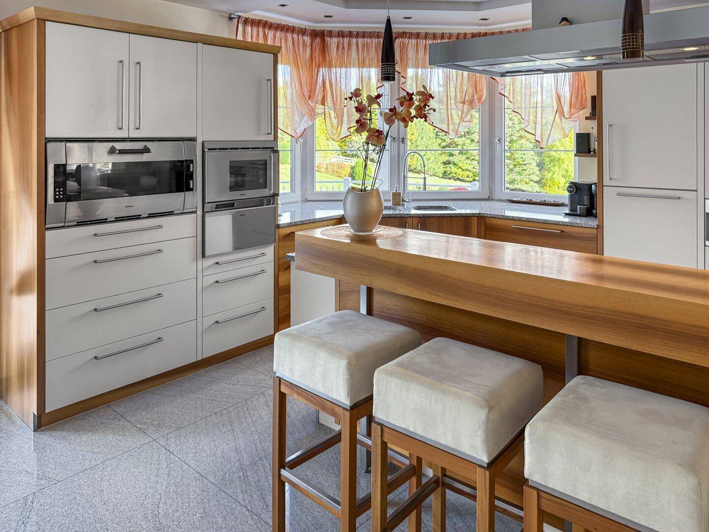 Helle Küche mit Holzelementen, Frühstücksbar, Einbaugeräten und Erkerfenster.