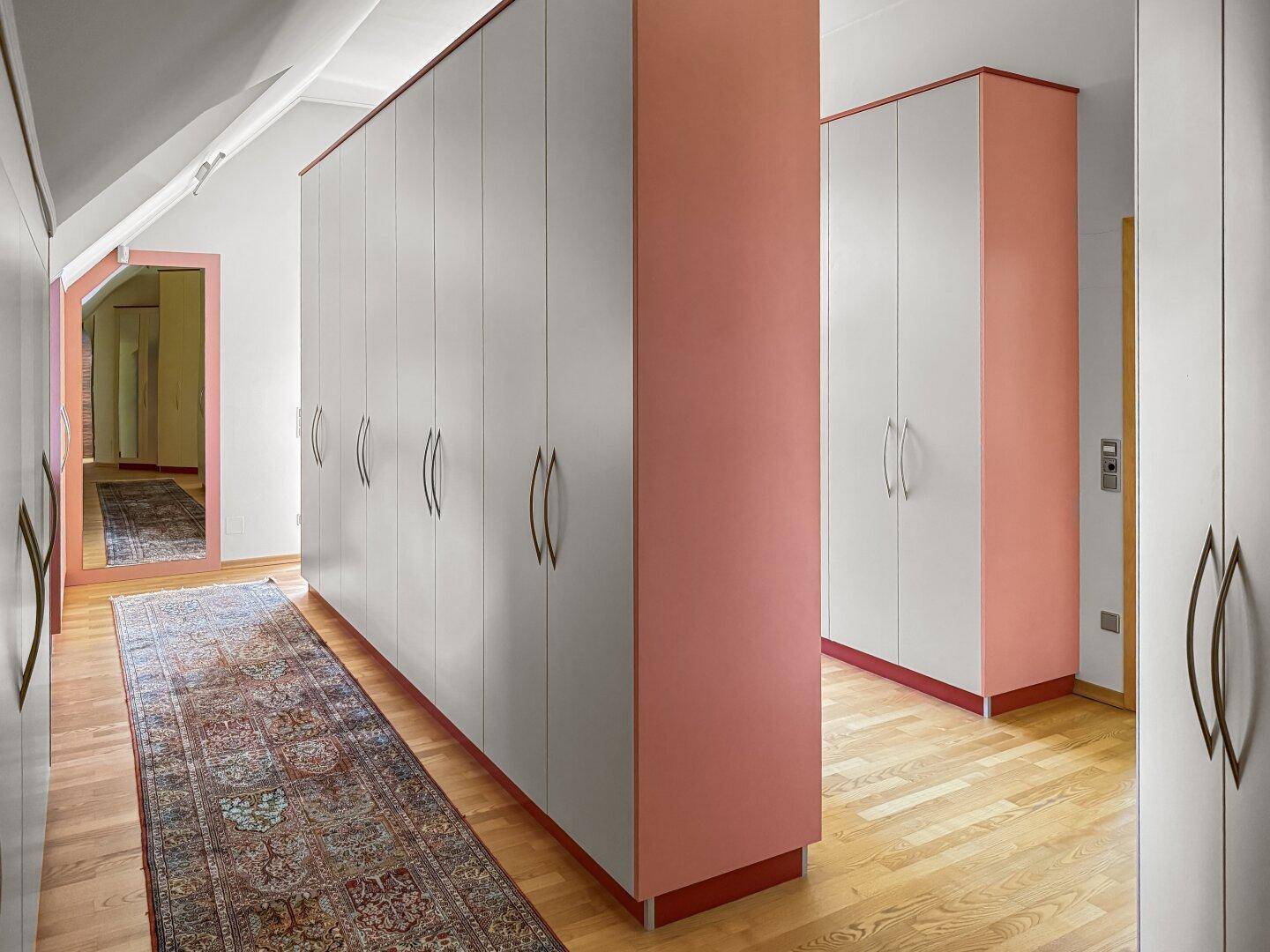 Begehbarer Kleiderschrank mit vielen Schränken und Teppich auf Holzboden.