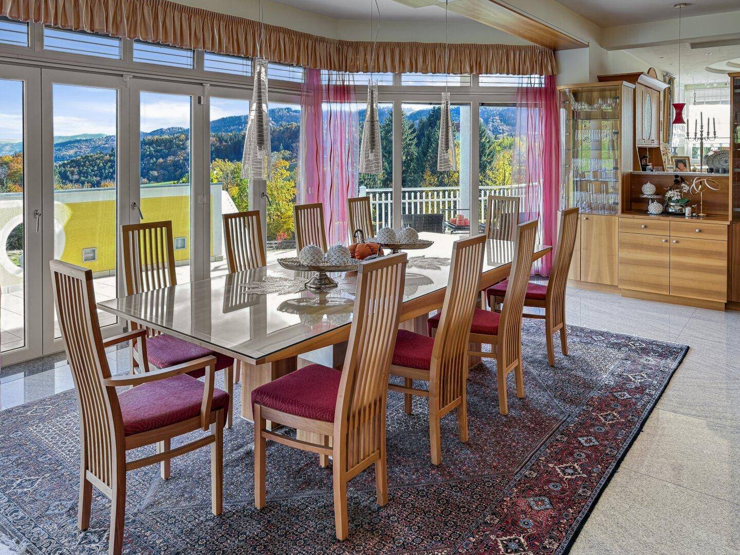Heller Essbereich mit großem Glastisch, Holzstühlen und Panoramablick auf die Landschaft.