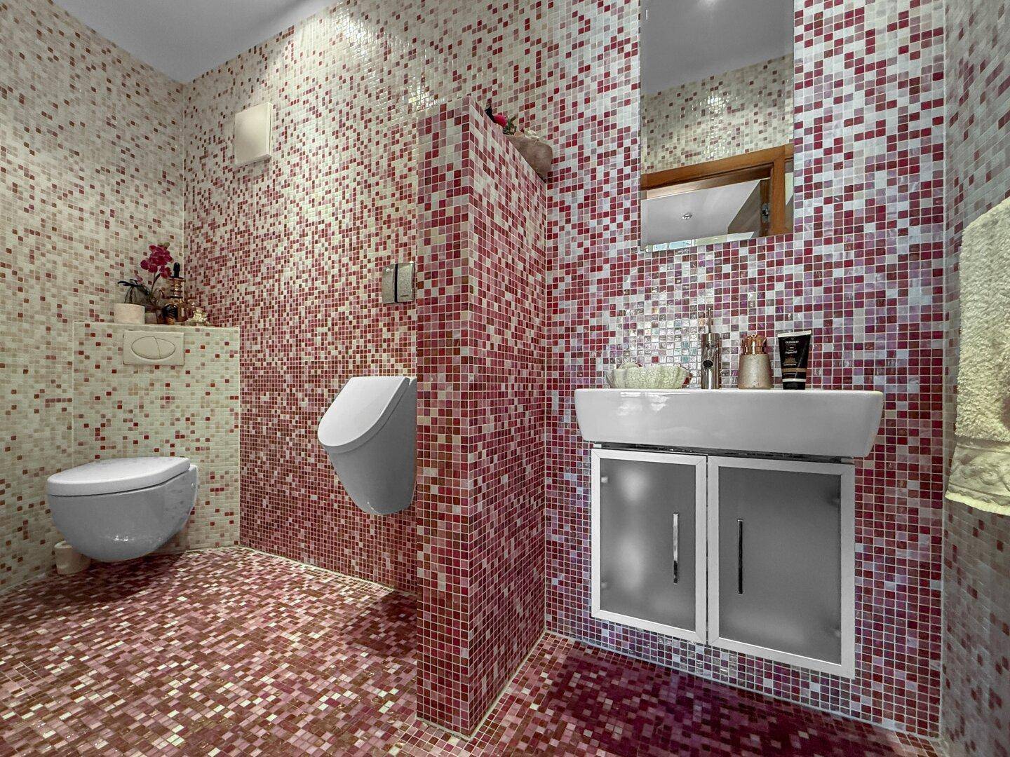 Modernes Badezimmer mit roten Mosaikfliesen, Wand-WC, Urinal und Waschbecken.