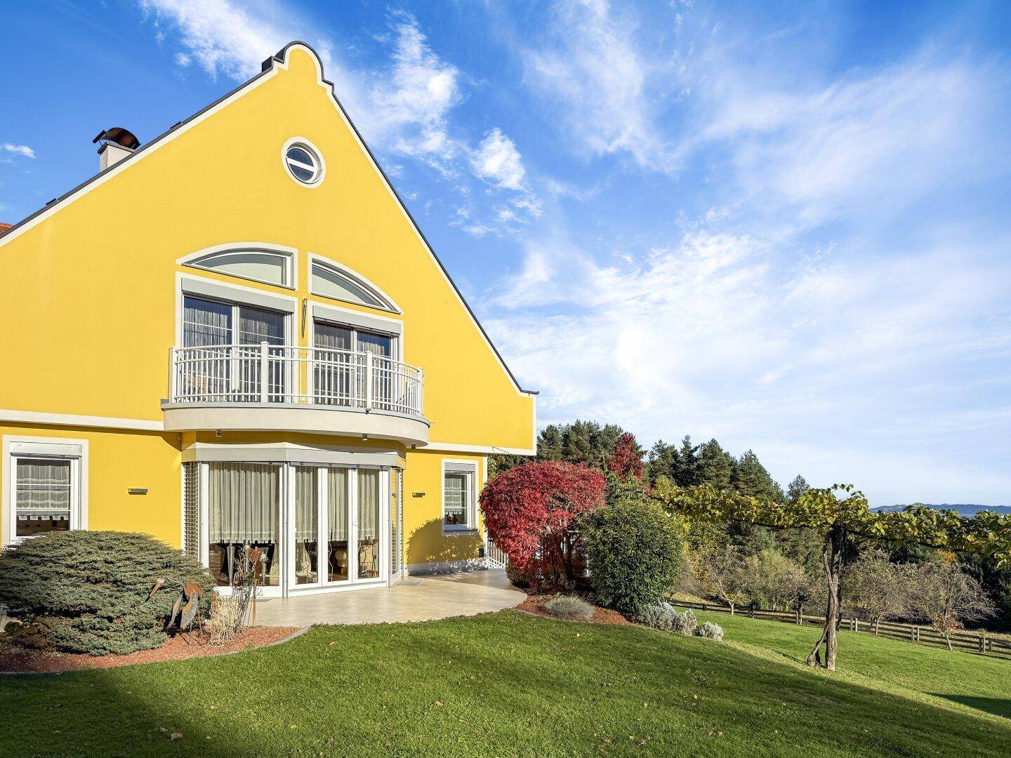 Gelbe Villa mit Balkon, Terrasse und gepflegtem Gartenbereich.