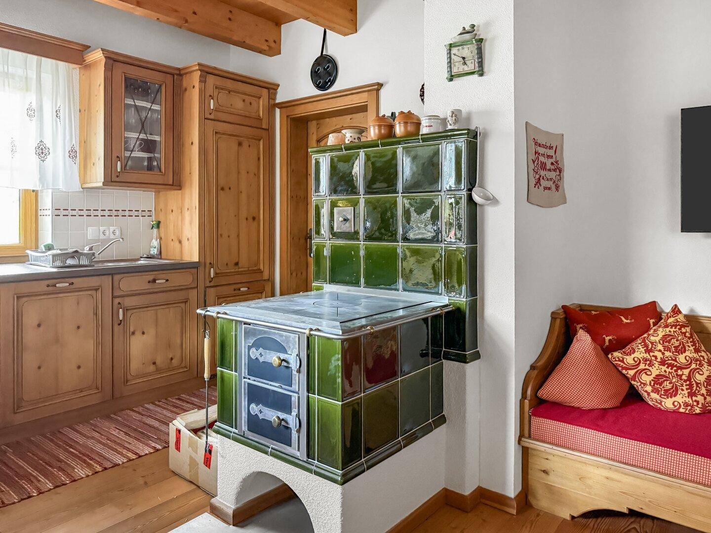 Rustikale Küche mit grünem Kachelofen, Holzschränken und Essecke.