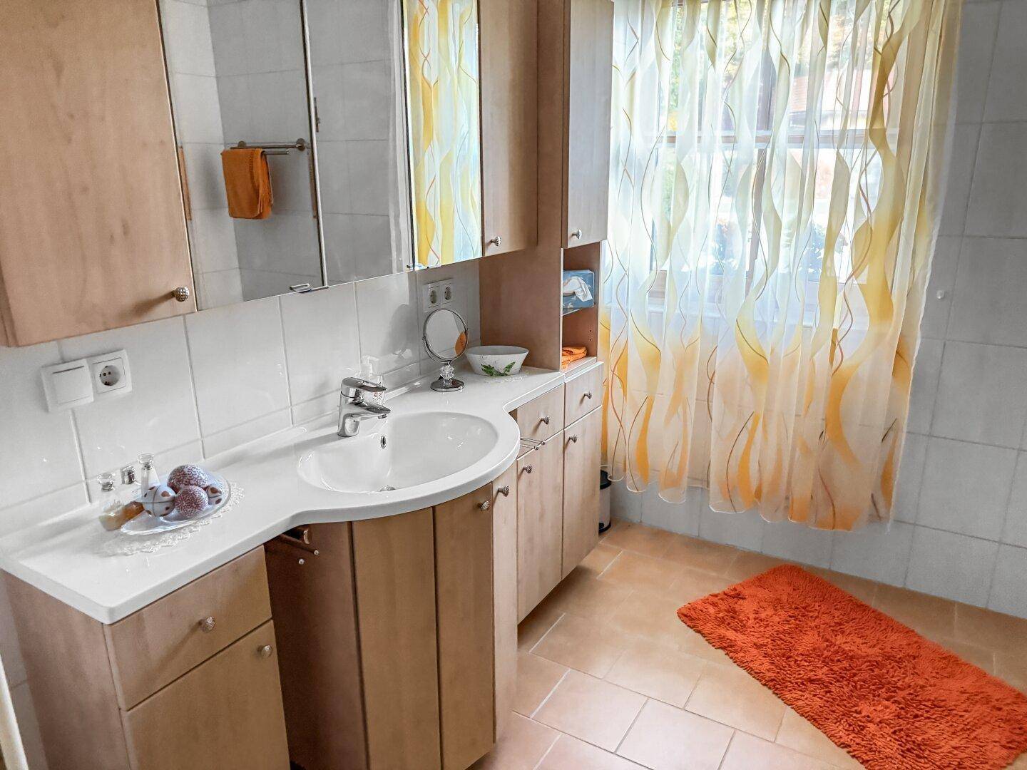 Badezimmer mit Einzelwaschbecken, Spiegelschrank und hellen Fliesen an Boden und Wänden.