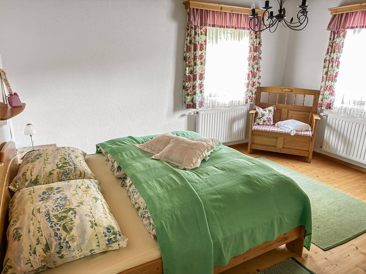 Schlafzimmer mit Holzbett, grüner Bettwäsche und floralen Vorhängen.