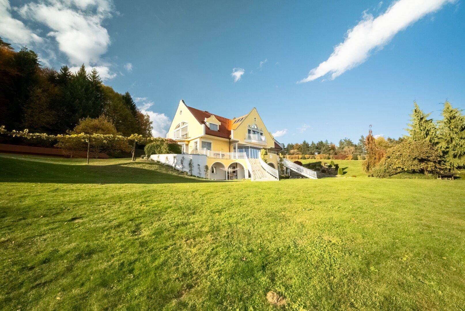Weitläufige Ansicht der gelben Villa mit großem Rasen und blauem Himmel.