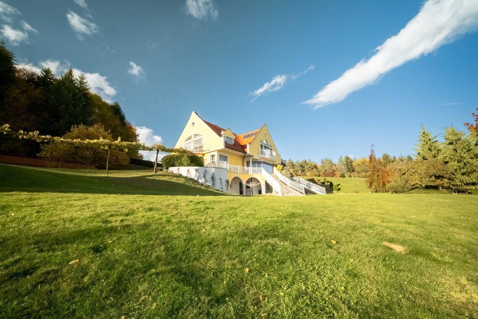 Weitläufige Ansicht der gelben Villa auf dem Hügel mit großem Rasen und blauem Himmel.