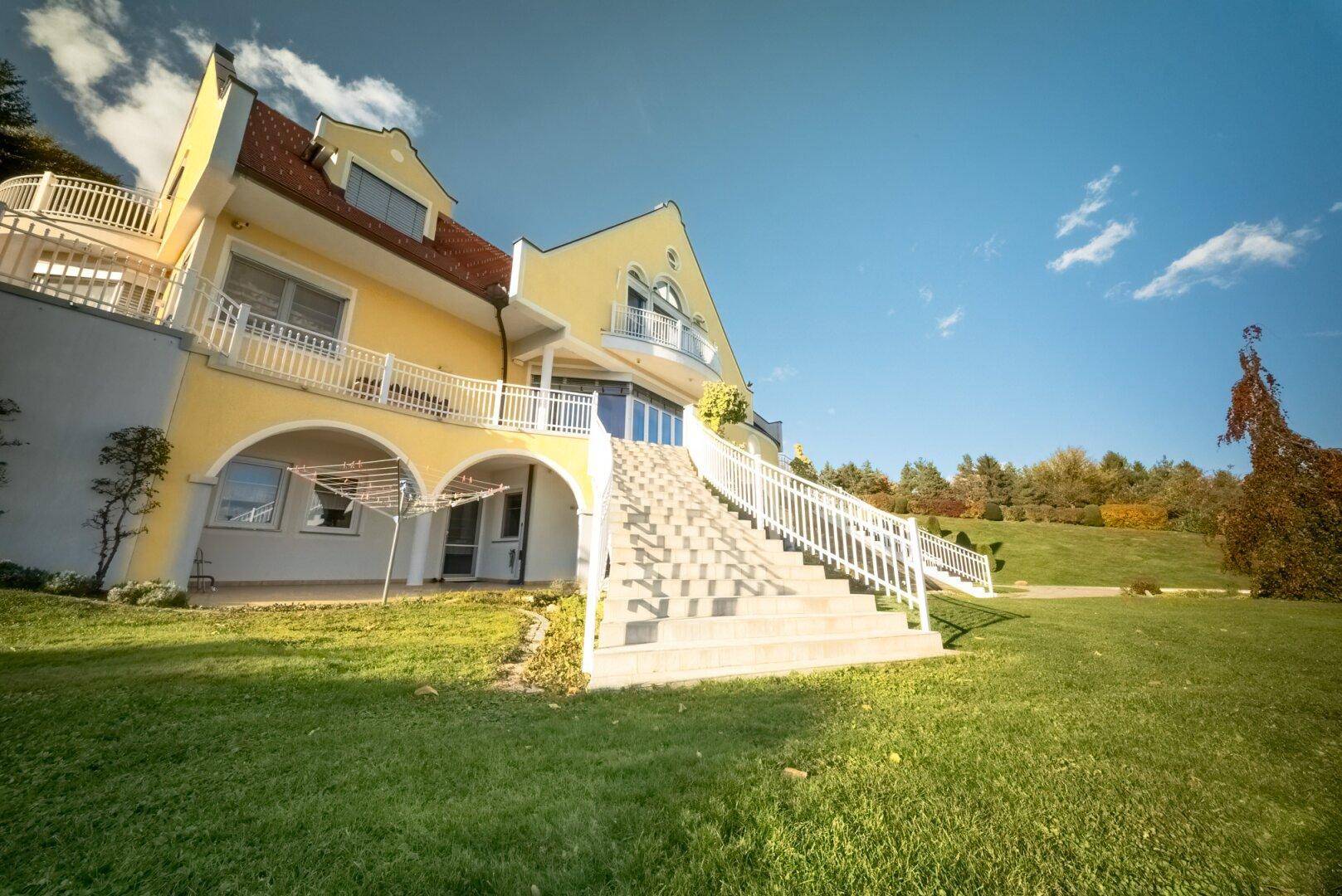Ansicht der gelben Villa von unten mit großer Freitreppe und mehreren Balkonen.