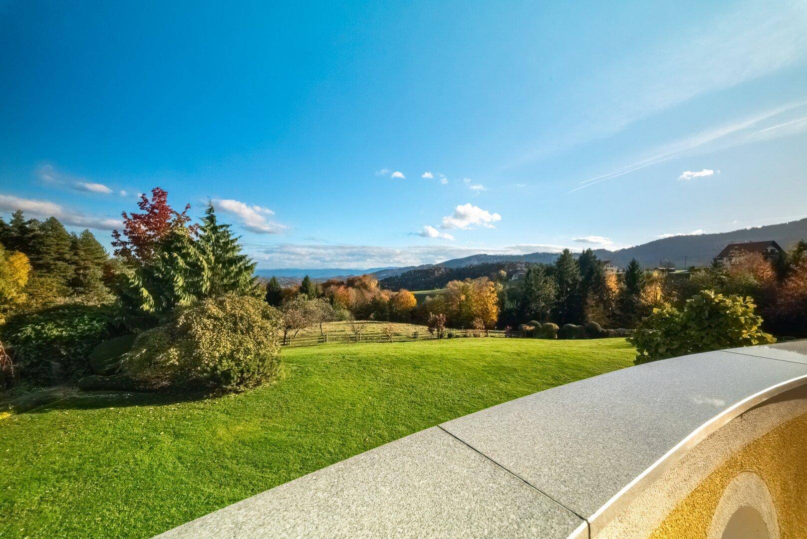 Weite Aussicht von der Terrasse auf die grüne Hügellandschaft und entfernte Bäume.