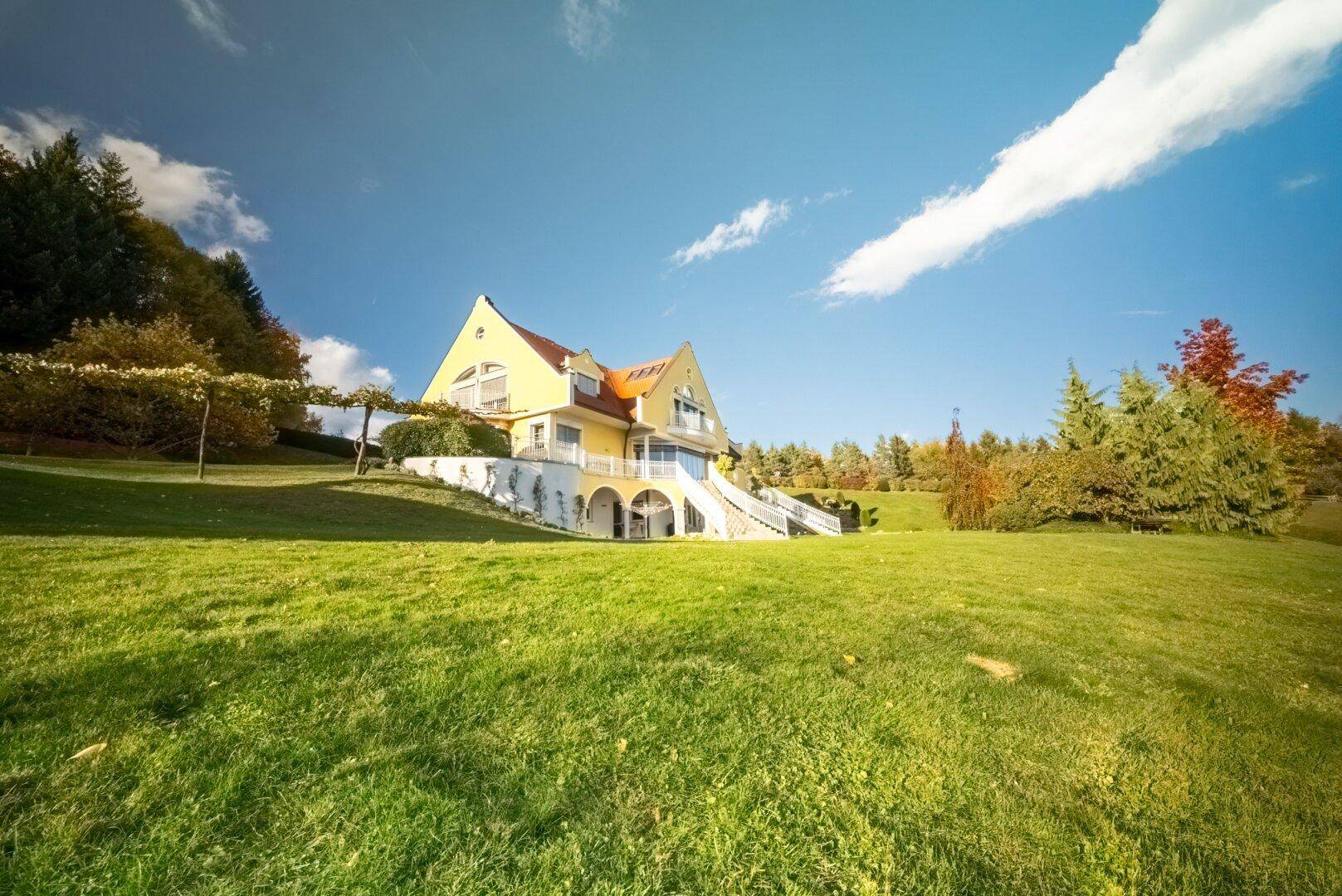 Gelbe Villa auf einem großen Rasengrundstück unter blauem Himmel.