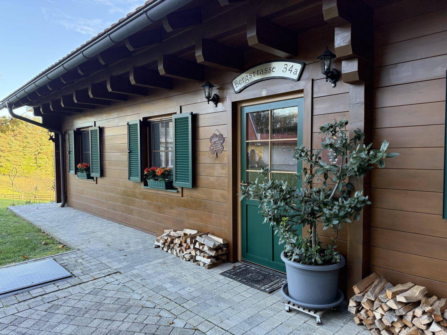 Eingangsbereich eines Holzhauses mit grüner Tür, Fensterläden und gestapeltem Brennholz.