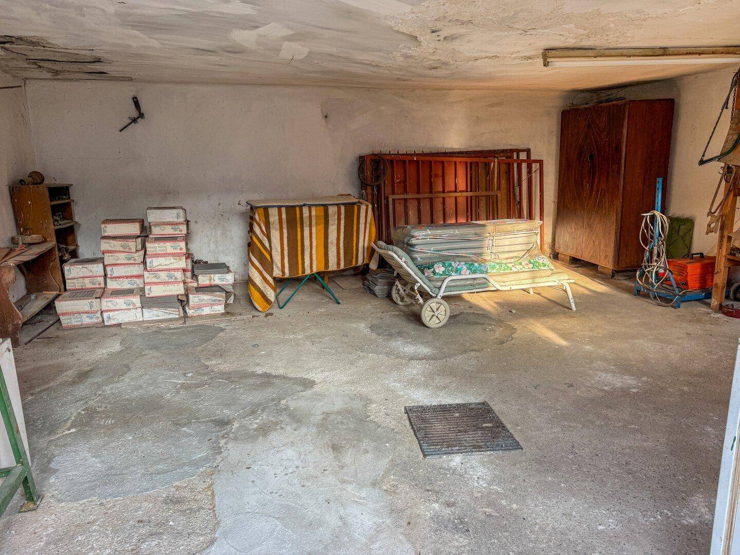 Geräumige Garage oder Abstellraum mit Betonboden und verschiedenen Lagergegenständen.