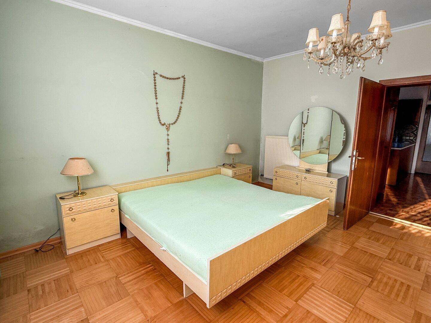 Geräumiges Schlafzimmer mit Doppelbett, Parkettboden und einem Kronleuchter an der Decke.
