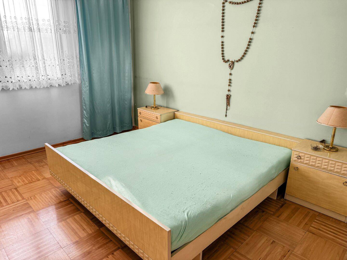 Schlafzimmer mit Doppelbett, Nachttischen und einem Fenster mit hellblauen Vorhängen.