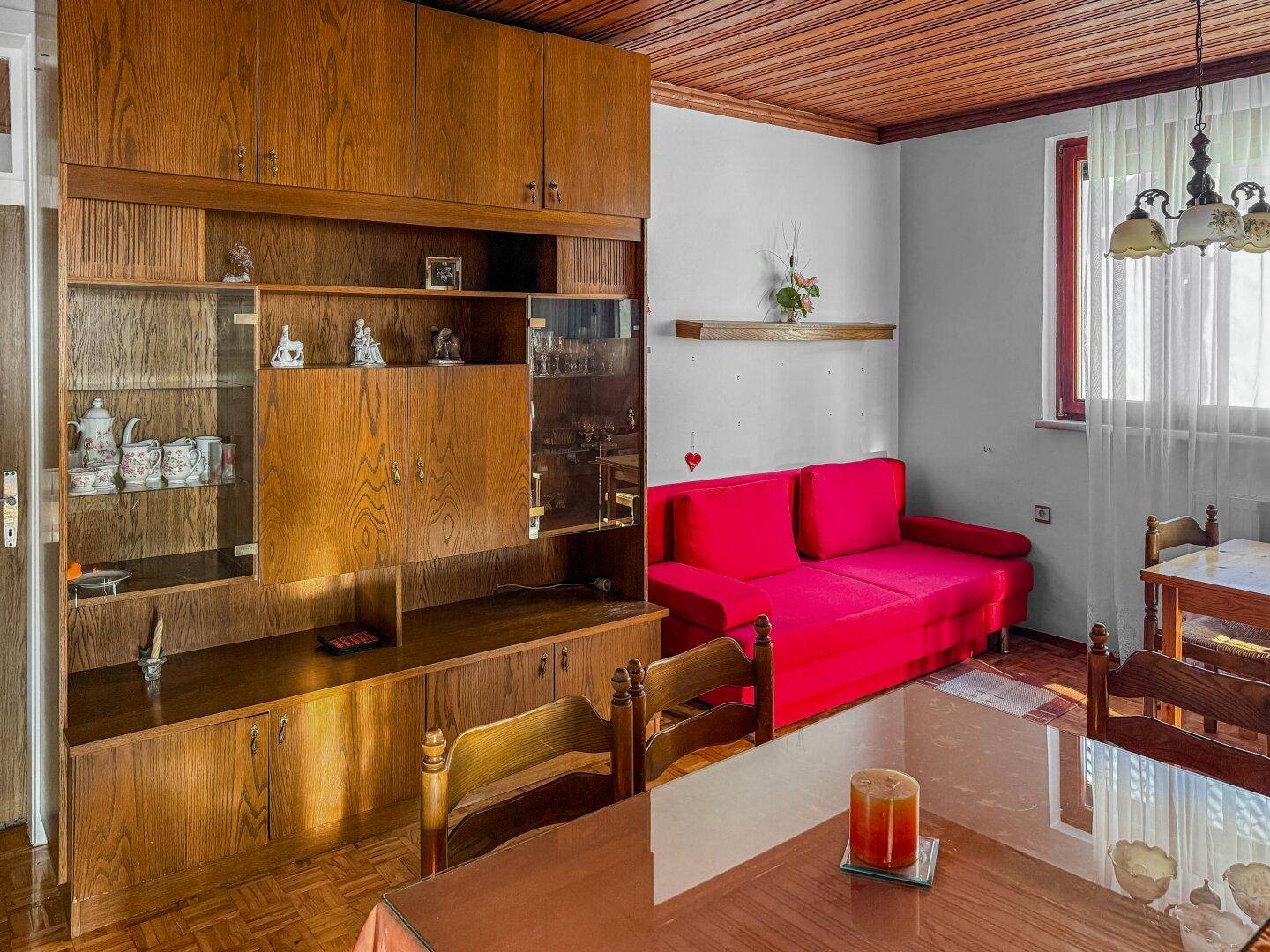 Wohnbereich mit rotem Sofa, Holzwandmöbeln und einem Esstisch, der zum Verweilen einlädt.