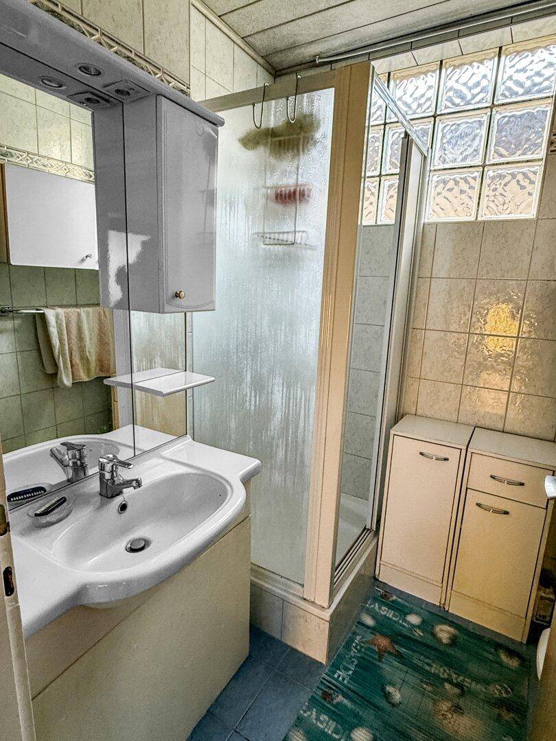 Badezimmer mit Dusche, Waschbecken und Fliesen an Wänden und Boden.