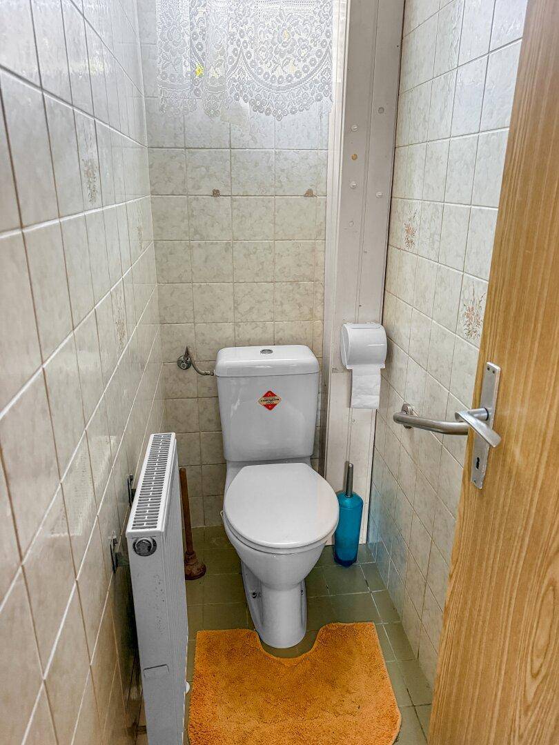 Kleines Gäste-WC mit Toilette, Heizkörper und Fliesen an den Wänden.