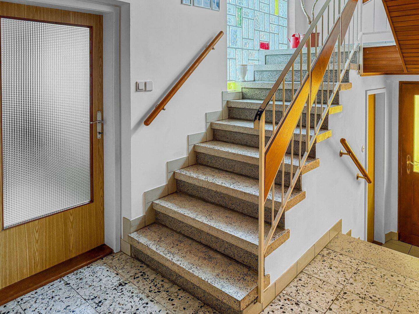 Treppenhaus mit Steinstufen, Holzgeländer und einem Fenster mit farbigem Glas.