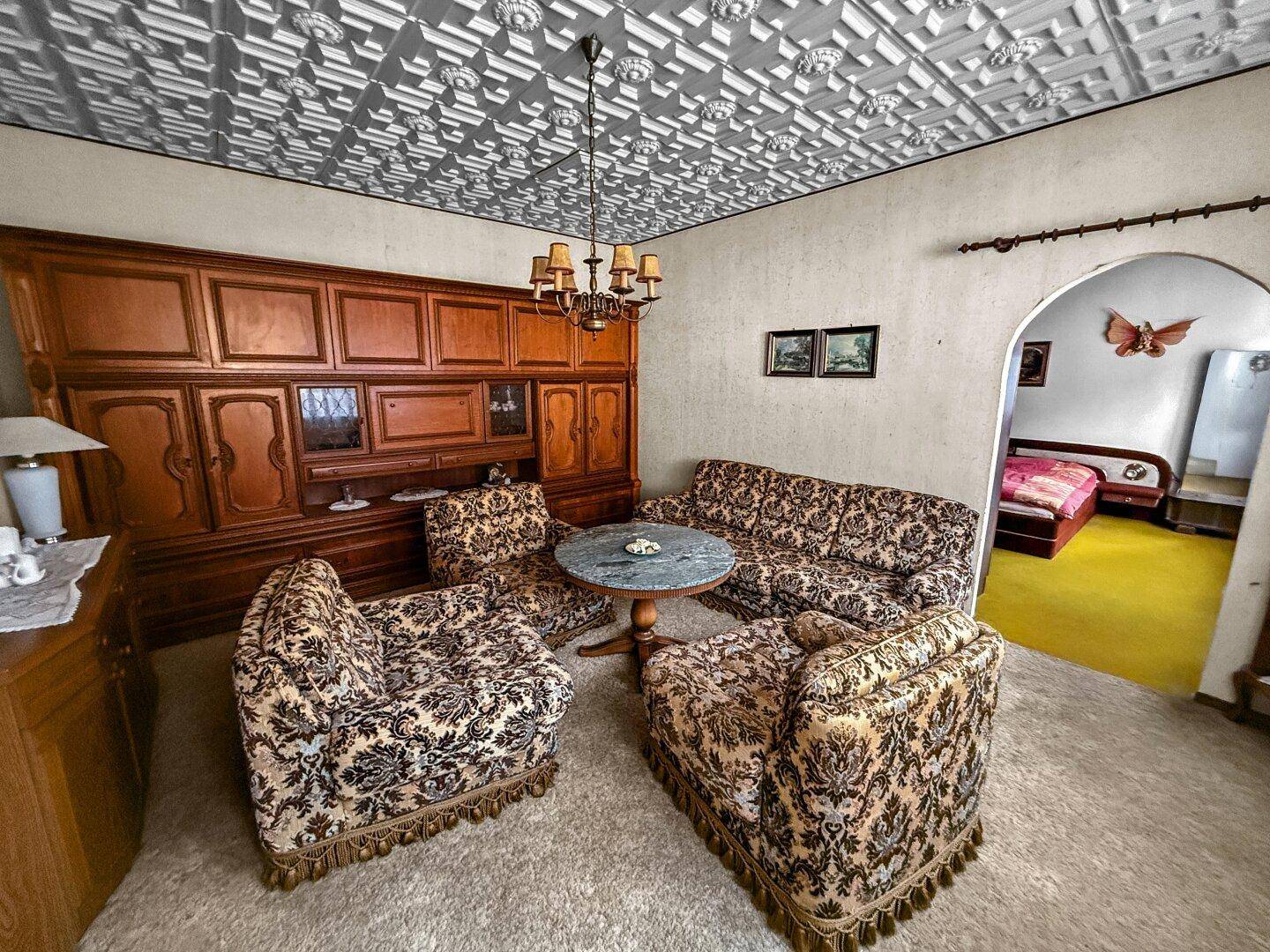 Traditionelles Wohnzimmer mit gemusterten Sofas, Holzwand und dekorativer Decke.