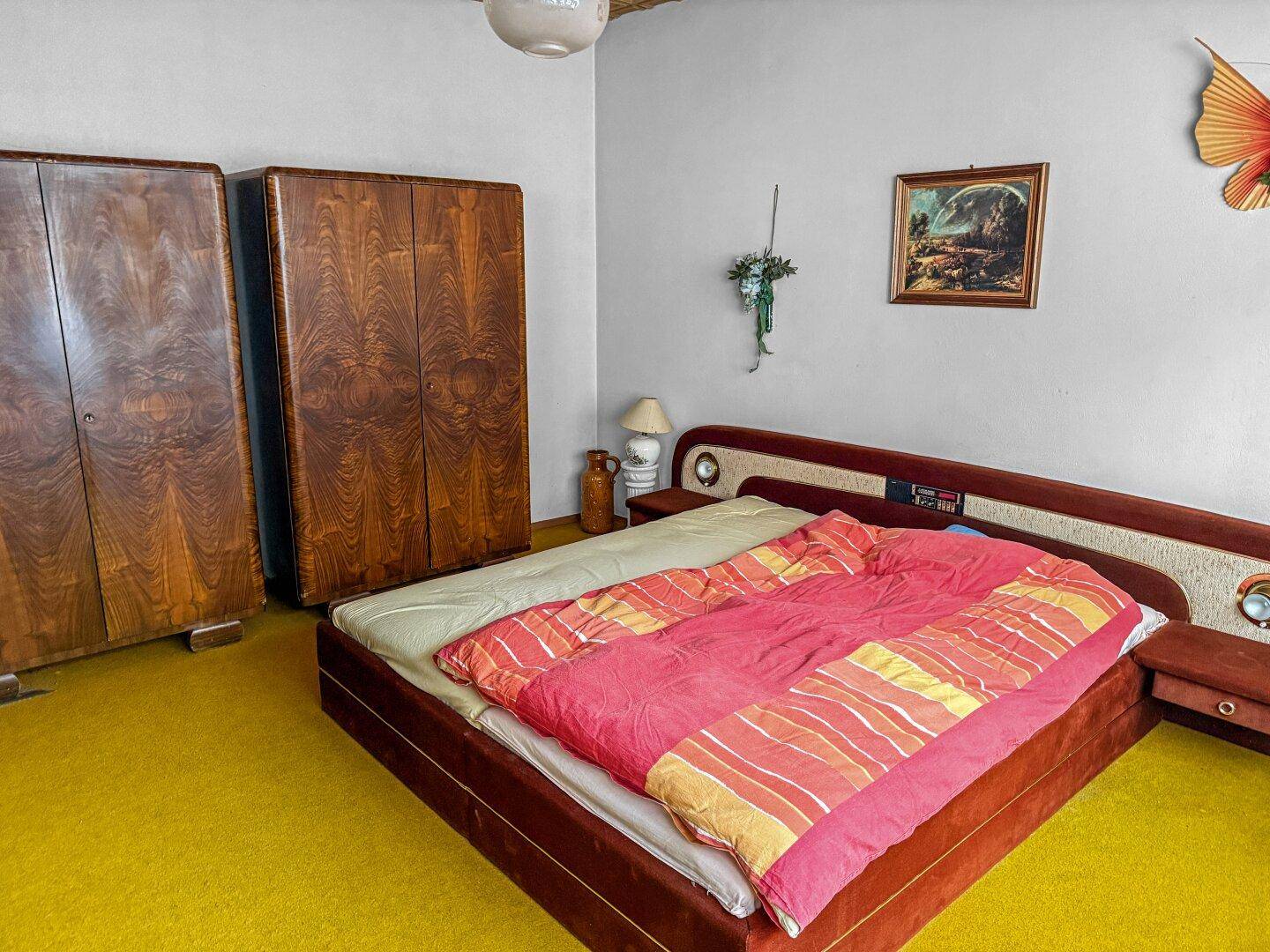 Schlafzimmer mit Doppelbett, Holzschränken und leuchtend gelbem Teppichboden.