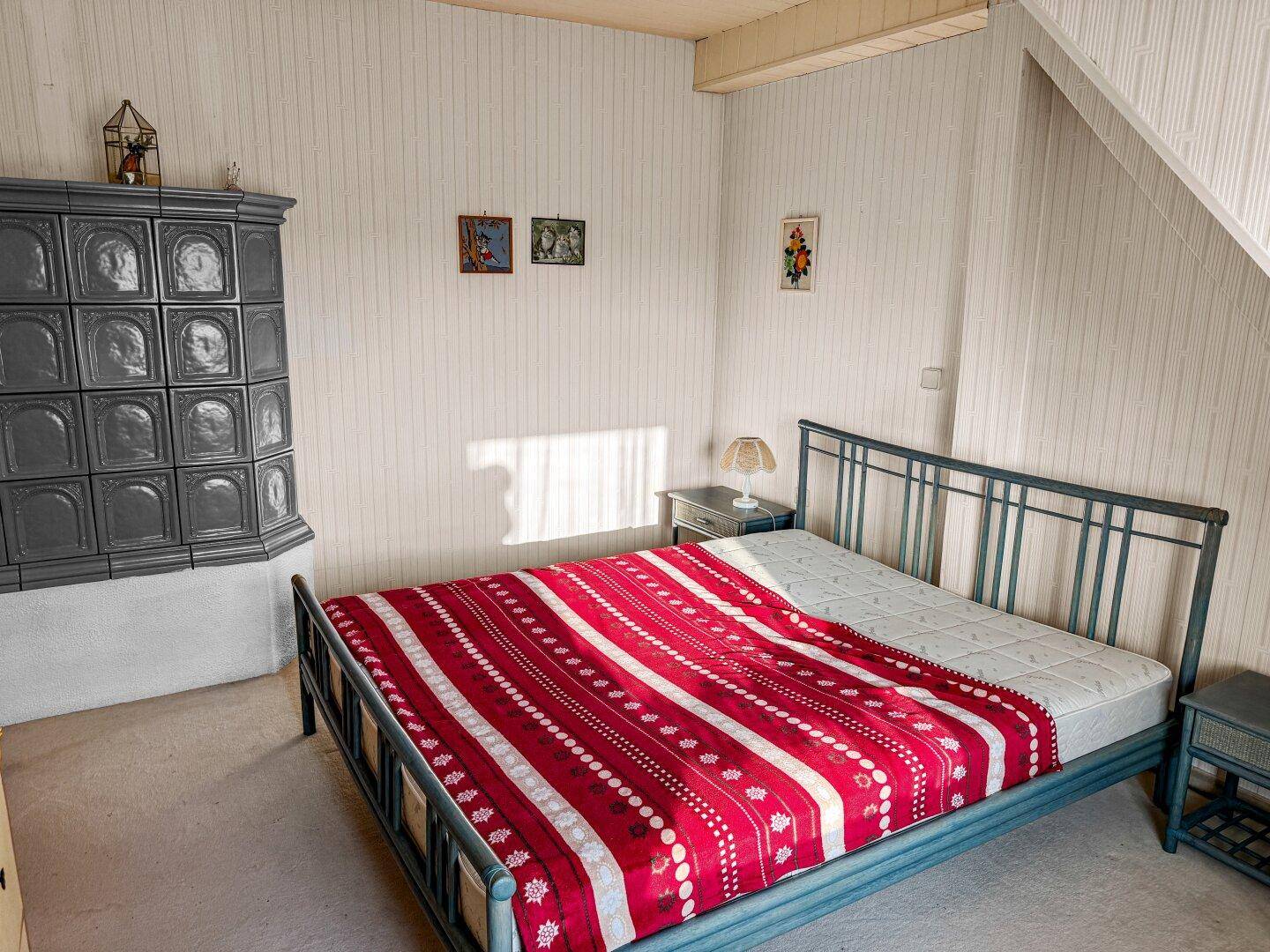 Schlafzimmer im Dachgeschoss mit Kachelofen, Metallbett und schrägen Wänden.