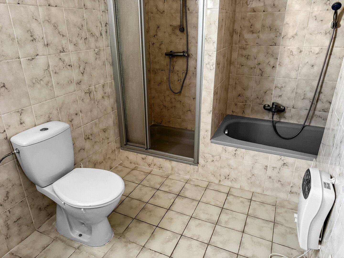 Badezimmer im Untergeschoss mit Dusche, Toilette und hellen Fliesen an Wänden und Boden.