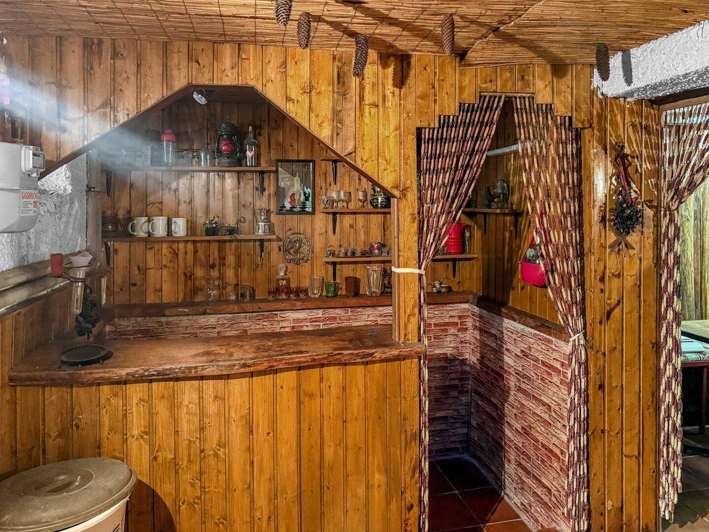 Rustikaler Barbereich im Keller mit Holzverkleidung, Ziegelakzenten und Regalen.