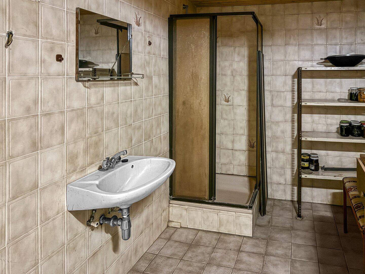 Einfaches Badezimmer im Keller mit Dusche, Waschbecken und hellen Fliesen.