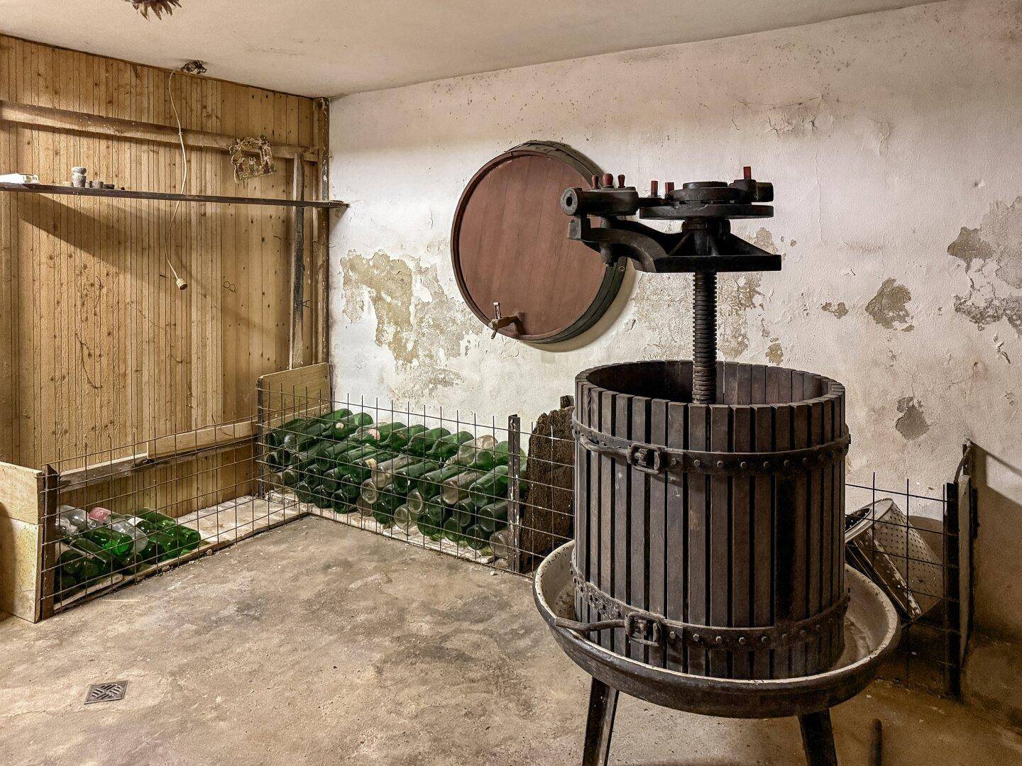 Traditioneller Weinkeller mit Holzpresse, Weinfässern und gelagerten Flaschen.