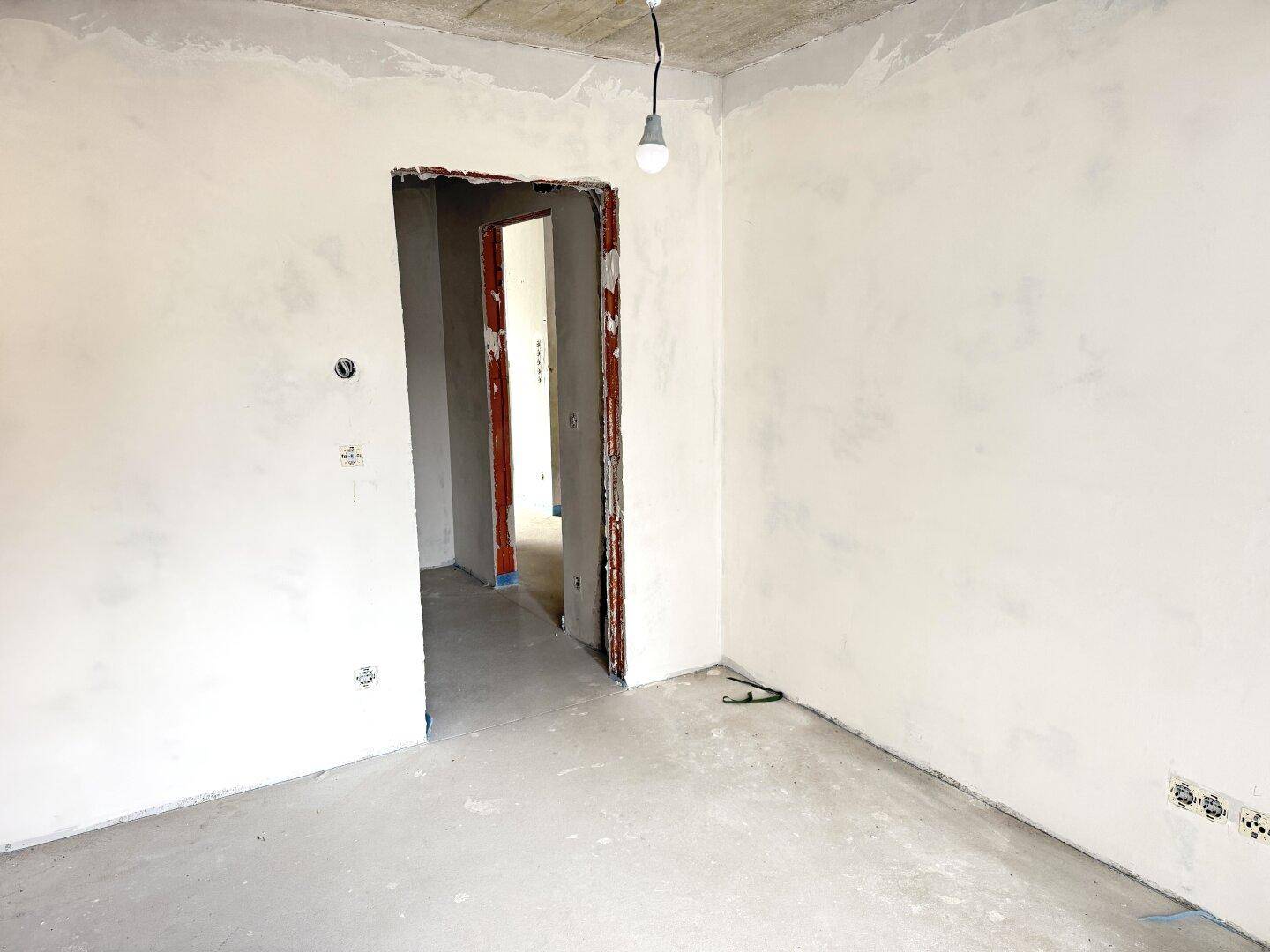 Unfertiger Innenraum im Rohbau mit Betonoberflächen und einem Türrahmen, bereit für den Ausbau.