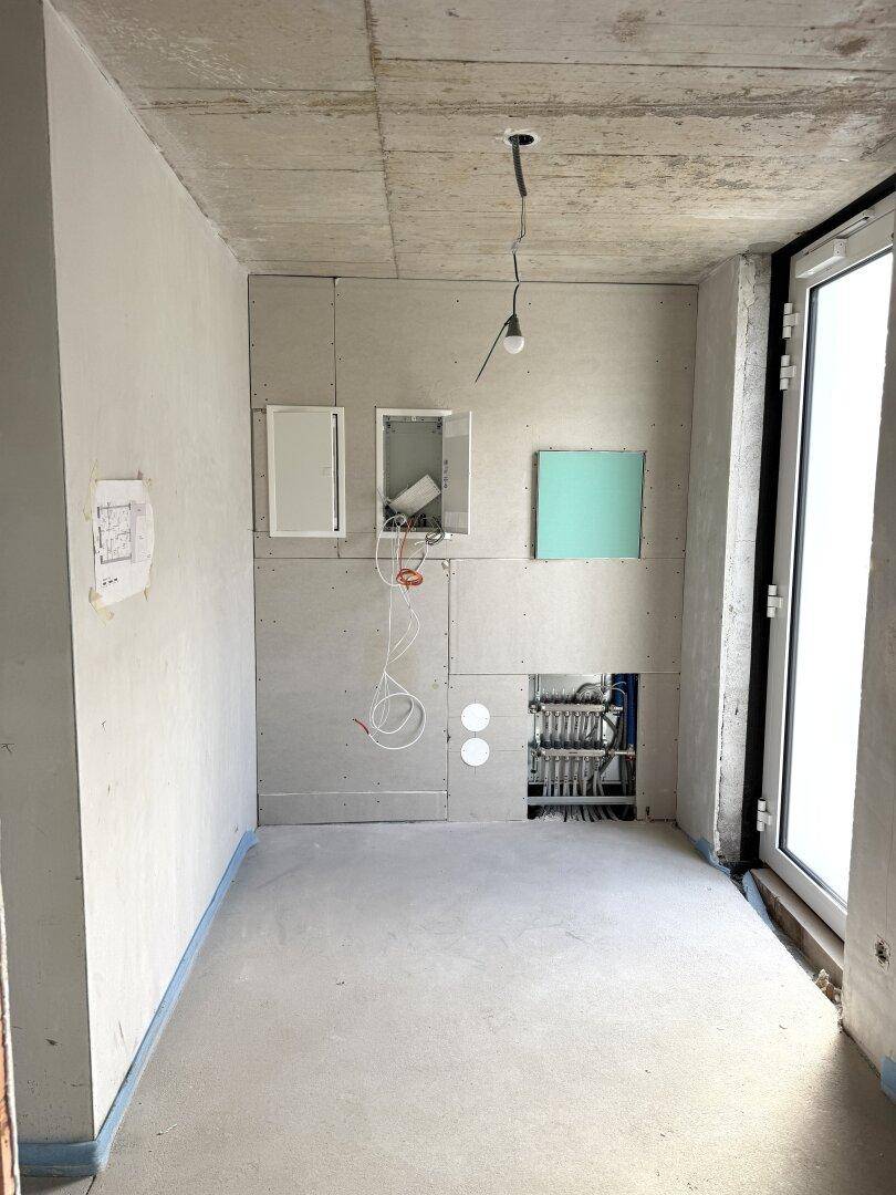 Rohbauzimmer mit vorbereiteten Installationen für Fußbodenheizung und einem großen Fenster oder Türöffnung.
