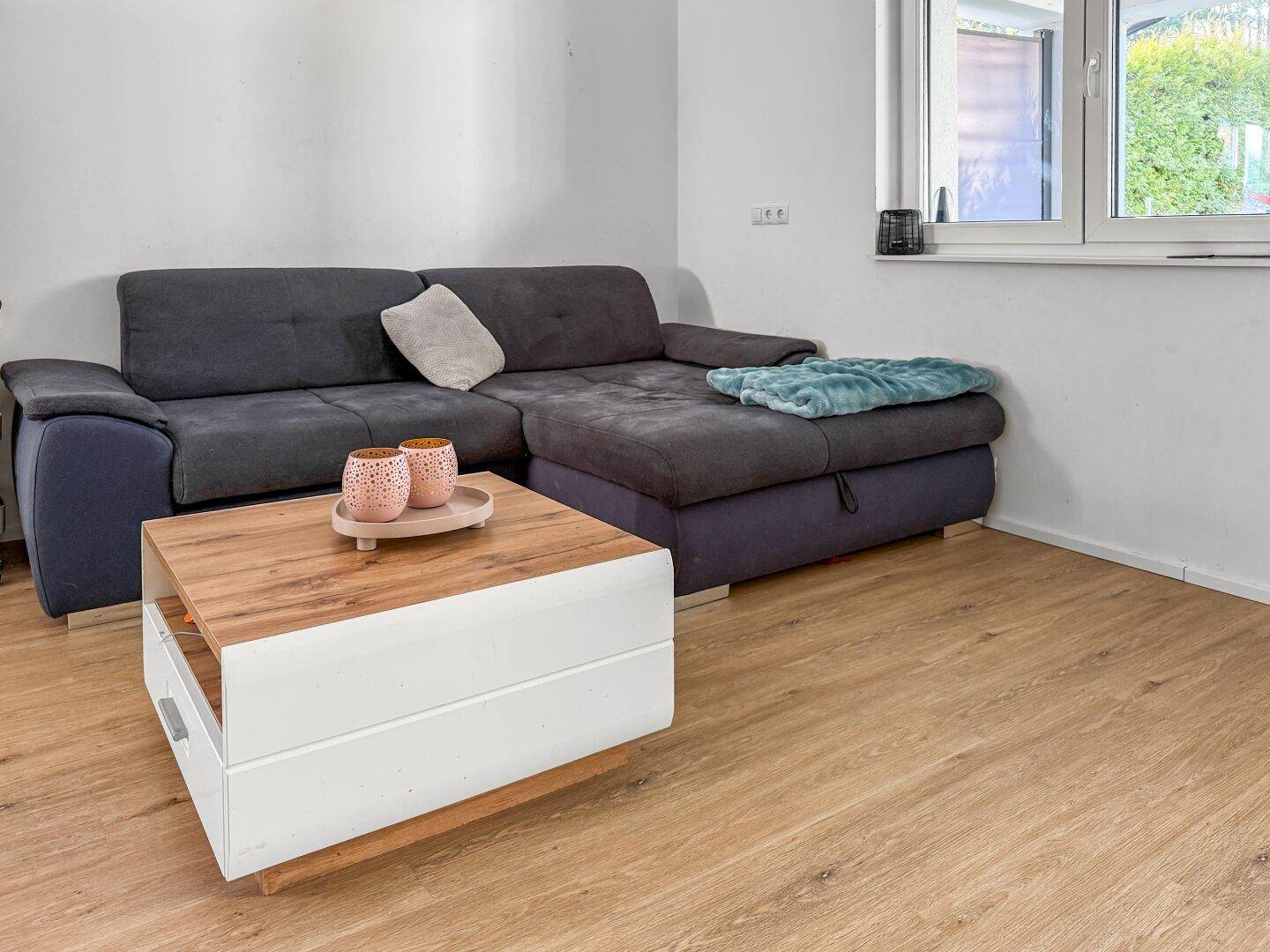 Gemütliches Wohnzimmer mit Ecksofa, modernem Couchtisch und hellem Laminatboden.