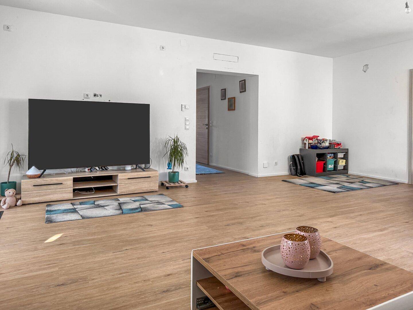 Geräumiges Wohnzimmer mit viel Tageslicht, Laminatboden und moderner Einrichtung.
