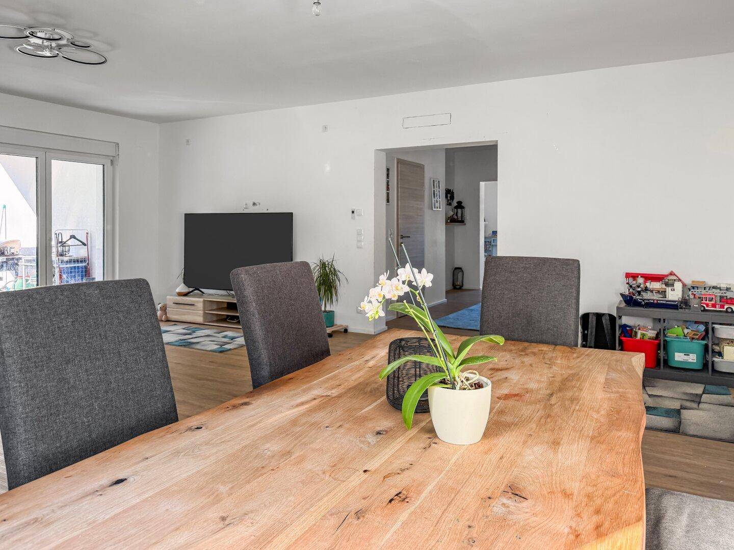 Offener Wohn- und Essbereich mit Holztisch, Stühlen und Zugang zum Balkon.